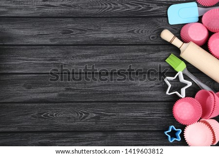 Pink cupcake cases with kitchen utensils on black wooden table