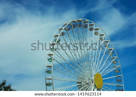 Multicolour ferris wheel on blue sky background, sunny summer weather, bright sun, happy day. Copy space, street photography.