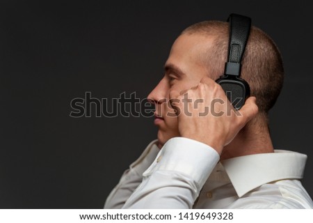 Side View - Young DJ guy listening to music in headphones to make a music set for a weekend of the party on the black background. Concept musical creative work
