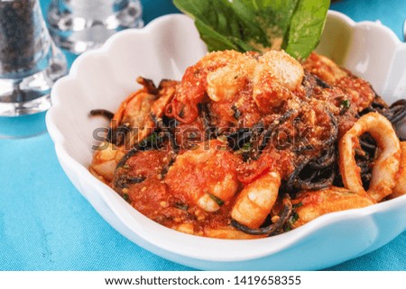 
Mediterranean dish, Georgian recipe. Black pasta with shrimps, crab meat, seafood, squid rings, basil, greens and cheese.