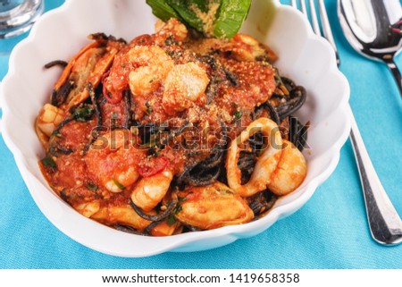 
Mediterranean dish, Georgian recipe. Black pasta with shrimps, crab meat, seafood, squid rings, basil, greens and cheese.