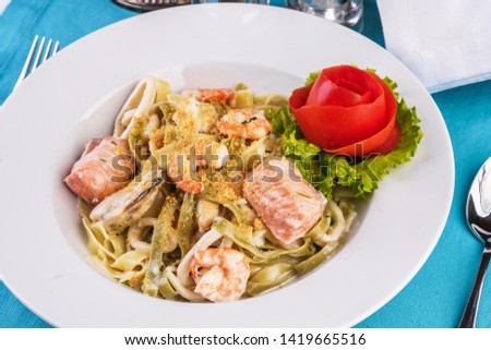 
Mediterranean dish, Georgian recipe. Creamy pasta with shrimps, crab meat, seafood, squid rings, tomatoes, basil, greens and cheese.