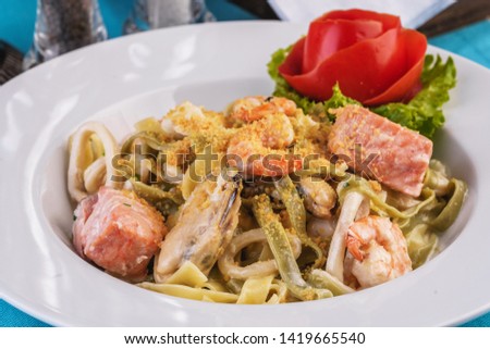 
Mediterranean dish, Georgian recipe. Creamy pasta with shrimps, crab meat, seafood, squid rings, tomatoes, basil, greens and cheese.