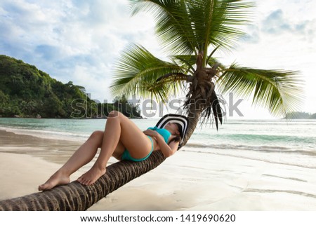 Young Woman In Bikini Lying On Palm Tree Over The Sand At Beach