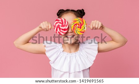 Little sweet tooth. Adorable girl covering her eyes with two colorful lollipops, pink panorama background Royalty-Free Stock Photo #1419691565