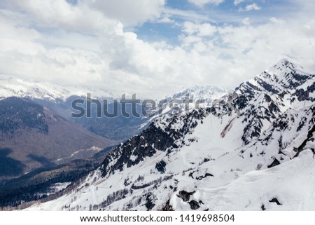 Beautiful snow-covered majestic mountain in a ski resort against a white lush cloud. The concept of rest in the ski resort and beautiful nature