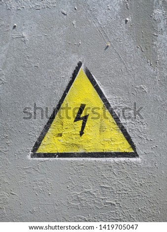sign of high voltage made by stencil and spray paint on a gray metal door painted in gray color
