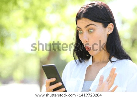 Surprised adult woman finds offers on smart phone standing in a park