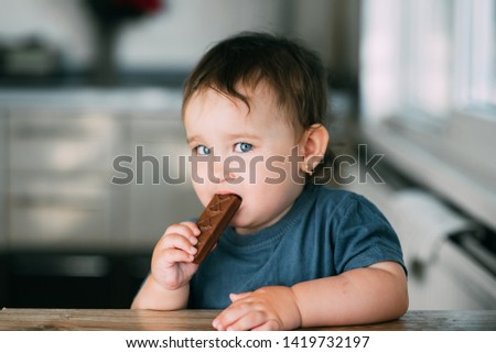 little beautiful girl in the afternoon in the kitchen eating a delicious chocolate bar