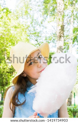 portrait of cute girl in hat eating cotton candy in park in summertime. summer vacation.