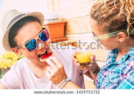 caucasian guy and adult woman at home in the terrace having breakfast together with a funny face of the teenager whil he's eating a bread with marmelade - boy with sunglasses having fun and joking