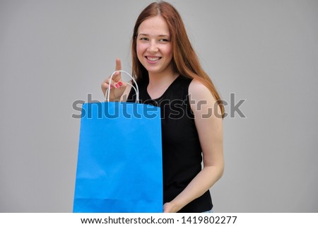 Photo portrait of a beautiful young pretty girl with dark red hair on a gray background in a black jacket. It should be with a blue package from the store in poses, smiling, happy with the purchase.