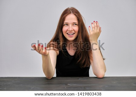 Photo portrait of a beautiful young pretty girl with dark red hair on a gray background in a black jacket. sHe sits at a dark table and talks in various poses, smiles. Made in a studio.