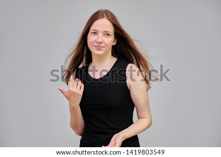 Photo portrait of a beautiful young pretty girl with dark red hair on a gray background in a black jacket. It stands directly in front of the camera in various poses, smiling. Made in a studio.