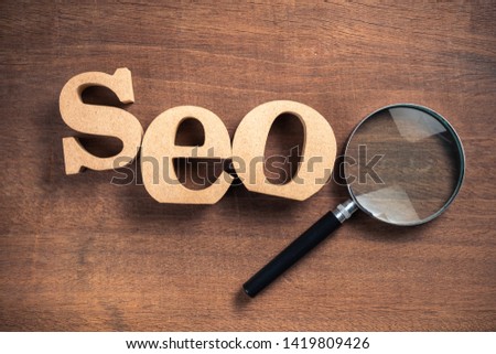 SEO (Search Engine Optimization) by wood letters with magnifying glass on wood background