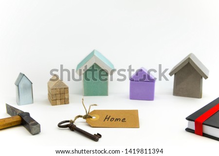 Five small houses made of different materials. Key with shield, hammer and book in the foreground.