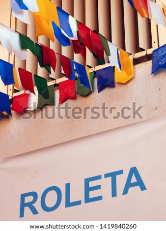 Banner in Portuguese says Roleta (roulette), common game of Junina Party, a traditional holiday in Brazil. Colorful flags background.