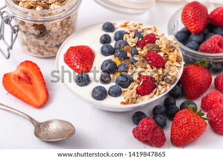 White yogurt in bowl with oatmeal and strawberries, blueberries and raspberries on the top on white background.