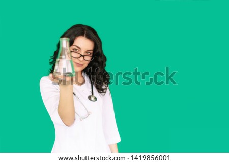 Girl nurse in the laboratory holding a flask, examines the contents, on a green screen background
