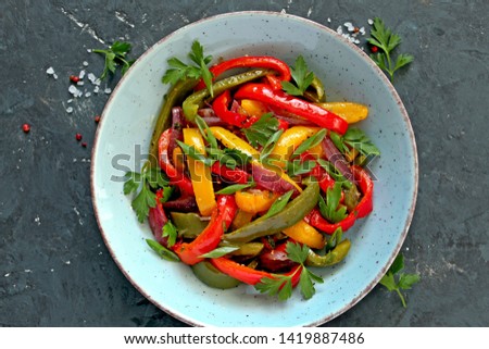 Roasted yellow, green and red bell pepper salad in a blue bowl with naan bread on dark background. Top view with copy space.