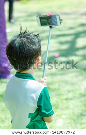 Happy little boy taking self photo in the summer park. Children and technology Concept. 