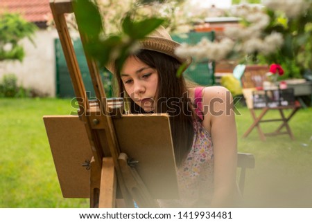 Portrait - Focused girl in straw hat at easel paints a picture outdoors
