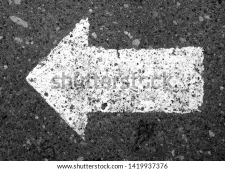 Left pointing arrow on asphalt in black and white. Signs and symbols.