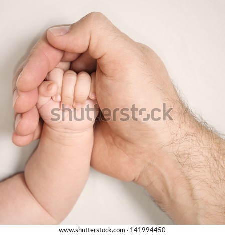 Adult's hand holding and protecting hand of baby - sepia tone picture