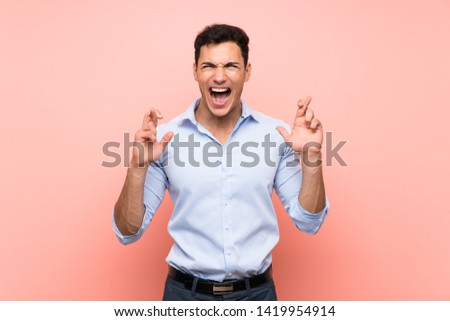 Handsome man over pink background with fingers crossing