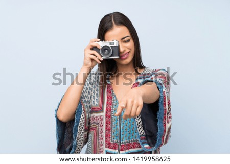 Young woman over isolated blue wall holding a camera