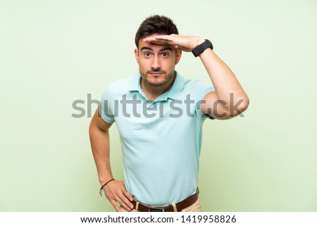 Handsome young man over isolated background looking far away with hand to look something
