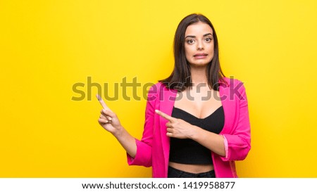 Young woman over isolated yellow background frightened and pointing to the side