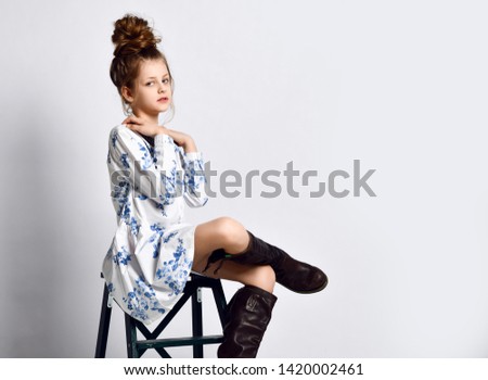 Beautiful fashionable kid girl in modern dress and big black boots posing on white background