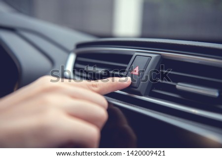 Finger hitting emergency light stop botton in the car , man pressing red triangle car hazard warning button.