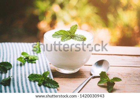 Natural flavored yogurt in clear glass cups, mint leaves on a blue background.  With mild sunlight in the morning
