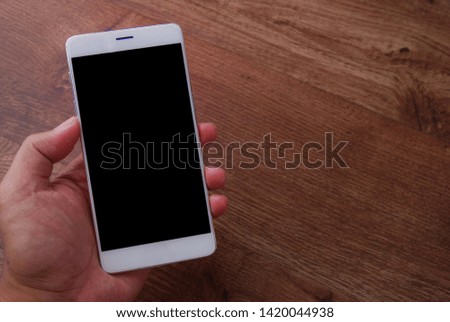 Man holding a white mobile phone with black screen isolated on wooden background