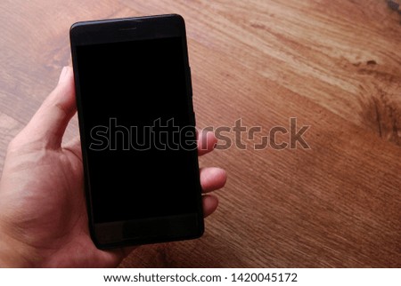 Man holding a black mobile phone with black screen isolated on wooden background