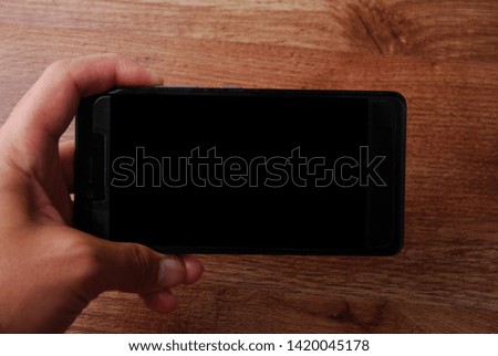 Man holding a black mobile phone with black screen isolated on wooden background