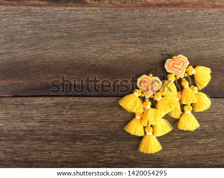 Handmade earring heart shape and yellow woven thread thai tradional fashion style on old wood texture background