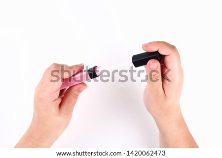 The girl holds in her hand a pink lip gloss on a white background. Top view.