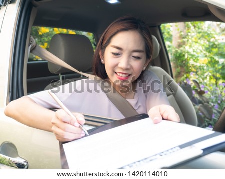 Asian woman inside car reading and signing insurance document.