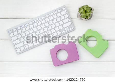 Office desk of blogger with camera, keyboard and plant on white wooden background top view