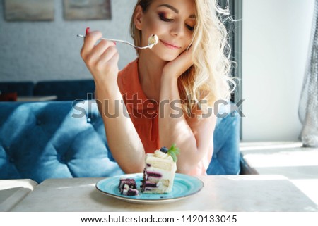 A beautiful woman in a cafe is drinking coffee and eating a cake. 