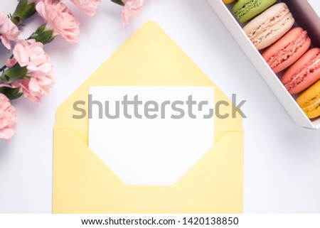 Yellow envelope with paper for text and beautiful carnation flowers with macaroons. Isolated.