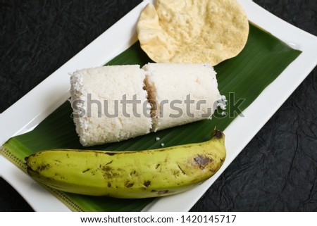 Popular South Indian steamed breakfast dish white Puttu or Pittu made of rice flour and grated coconut  in the bamboo mould with banana and Pappad Kerala, India. Sri lankan food served in banana leaf.