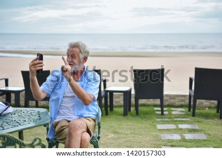 Portrait caucasian elder, senior mature man holding smartphone with green screen on tropical beach background