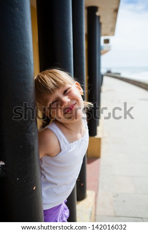 Smiling young girl between structural pillars alongside beachside walkway