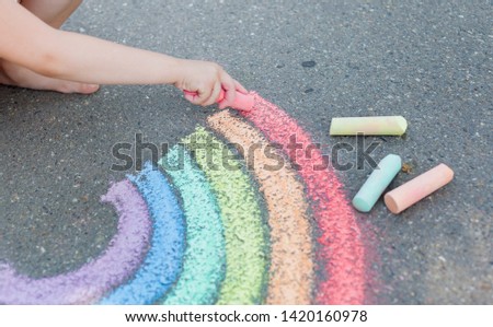  Kids paint outdoors. Portrait of a child girl drawing  a rainbow colored chalk on the asphalt on summer sunny day. Creative development of children