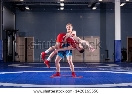 Two young men in blue and red wrestling tights are wrestlng and making a suplex wrestling on a yellow wrestling carpet in the gym. The concept of fair wrestling