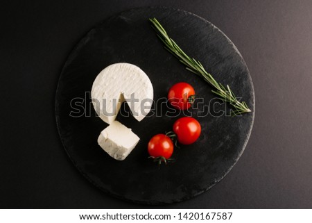 Salted soft cheese with cherry tomatoes on black background.